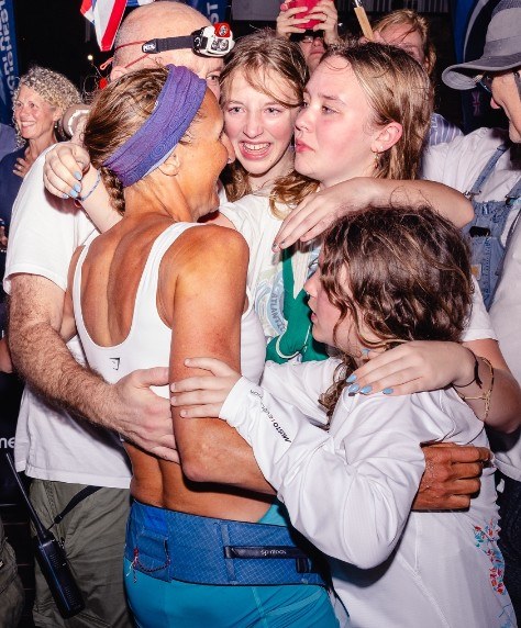 Sally is pictured wearing a white t-shirt and bandana and standing in the arms of three young members of her family who look excited to see her.
