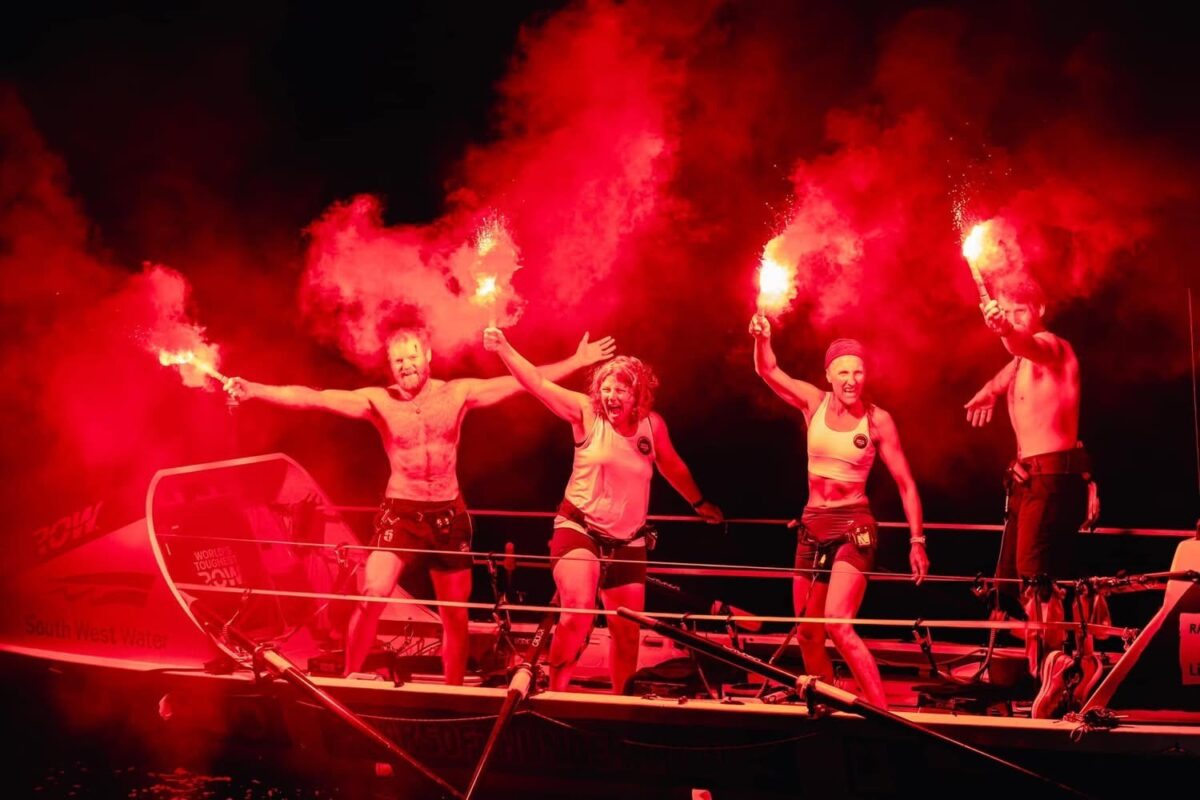 Sally and crew mates standing on their boat and holding flares celebrating the end of the row