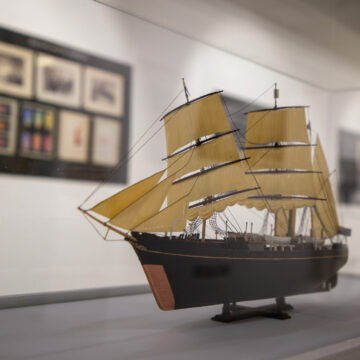 a model boat, on a stand in a gallery.