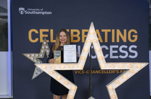 A person standing behind a large star, holding a certificate and smiling at the camera.