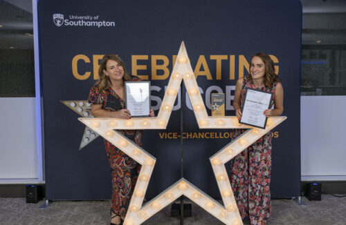 Two people kneeling and standing around a large star, holding certificates and smiling at the camera.