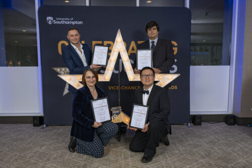 Four people kneeling and standing around a large star, holding certificates and smiling at the camera.