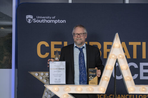 A person standing behind a large star, holding a certificate and smiling at the camera.