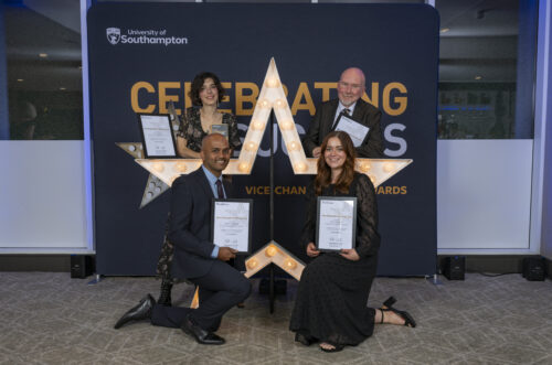 Four people kneeling and standing around a large star, holding certificates and smiling at the camera.