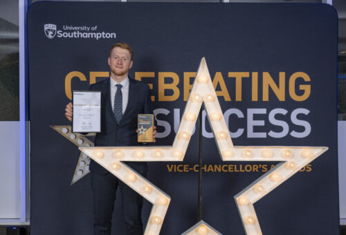A person standing behind a large star, holding a certificate and smiling at the camera.