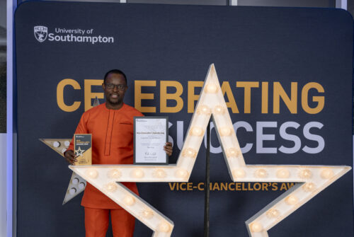 A person standing behind a large star, holding a certificate and smiling at the camera.