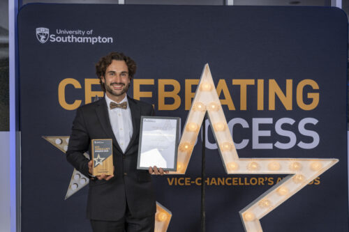 A person standing behind a large star, holding a certificate and smiling at the camera.