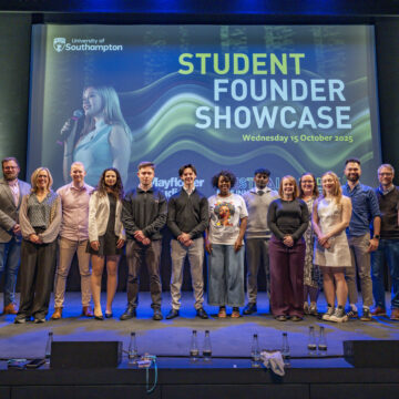 A group of people are stood in a line on stage, in front of a screen.