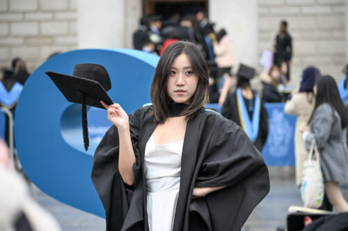 A woman poses confidently, with one hand on her hip and the other tipping her mortarboard.