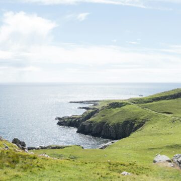 A landscape of green cliffs facing the sea, under a blue sky.