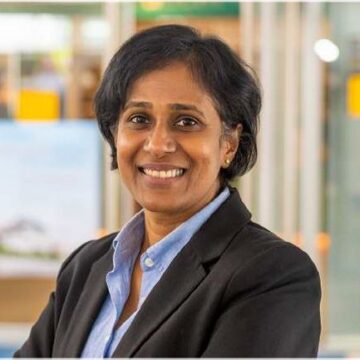 A woman with short black hair and wearing a blue shirt with black blazer, smiles