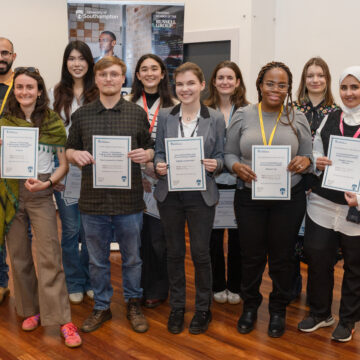 A group of people, stood in two rows, smiling and holding up certificates.