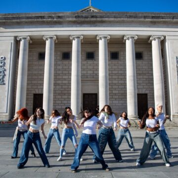 A group of people in white t-shirts and jeans are dancing outside the O2 Guildhall in Southampton.