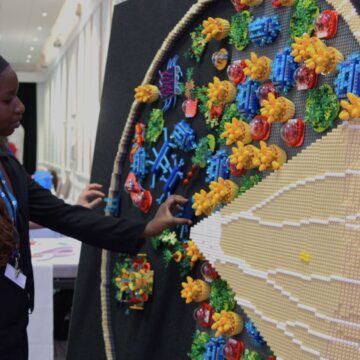A woman wearing a black headband is adding a piece toa big Lego sculpture.