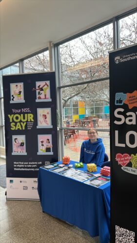 Student Ambassador near their NSS stand smiling at the camera