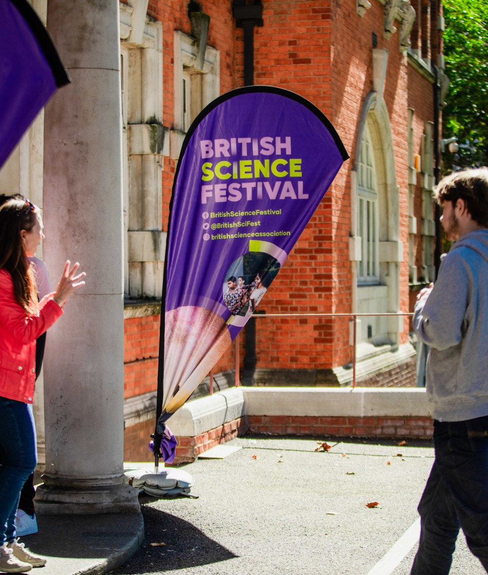 Two people are looking towards a pop-up banner that reads British Science Festival