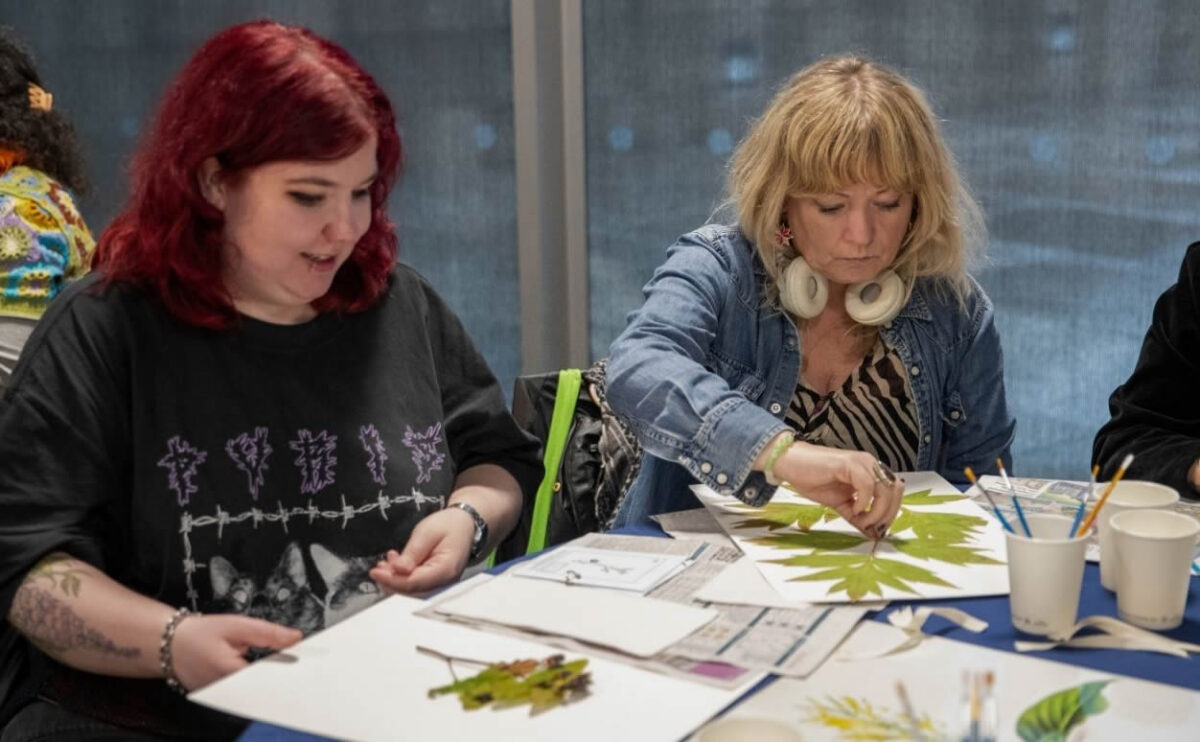 Two women, one with red and the other with blonde hair, sat doing crafts with leaves.