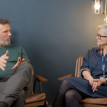A man and woman, both sat on chairs, having a conversation.