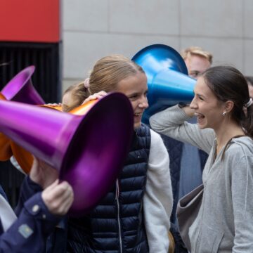 3 people are holding multi-coloured funnels up to their ears and laughing