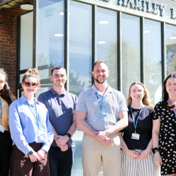 A team of six people are stood outside The Hartley Library, smiling.