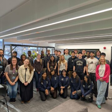 A large group of young people are smiling, posing for a photo inside a common room.