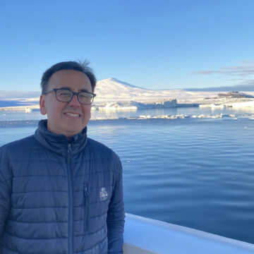 A man, wearing a coat, is stood in front of a snowy landscape.