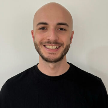 A bald man with a beard is wearing a black t-shirt and smiling.