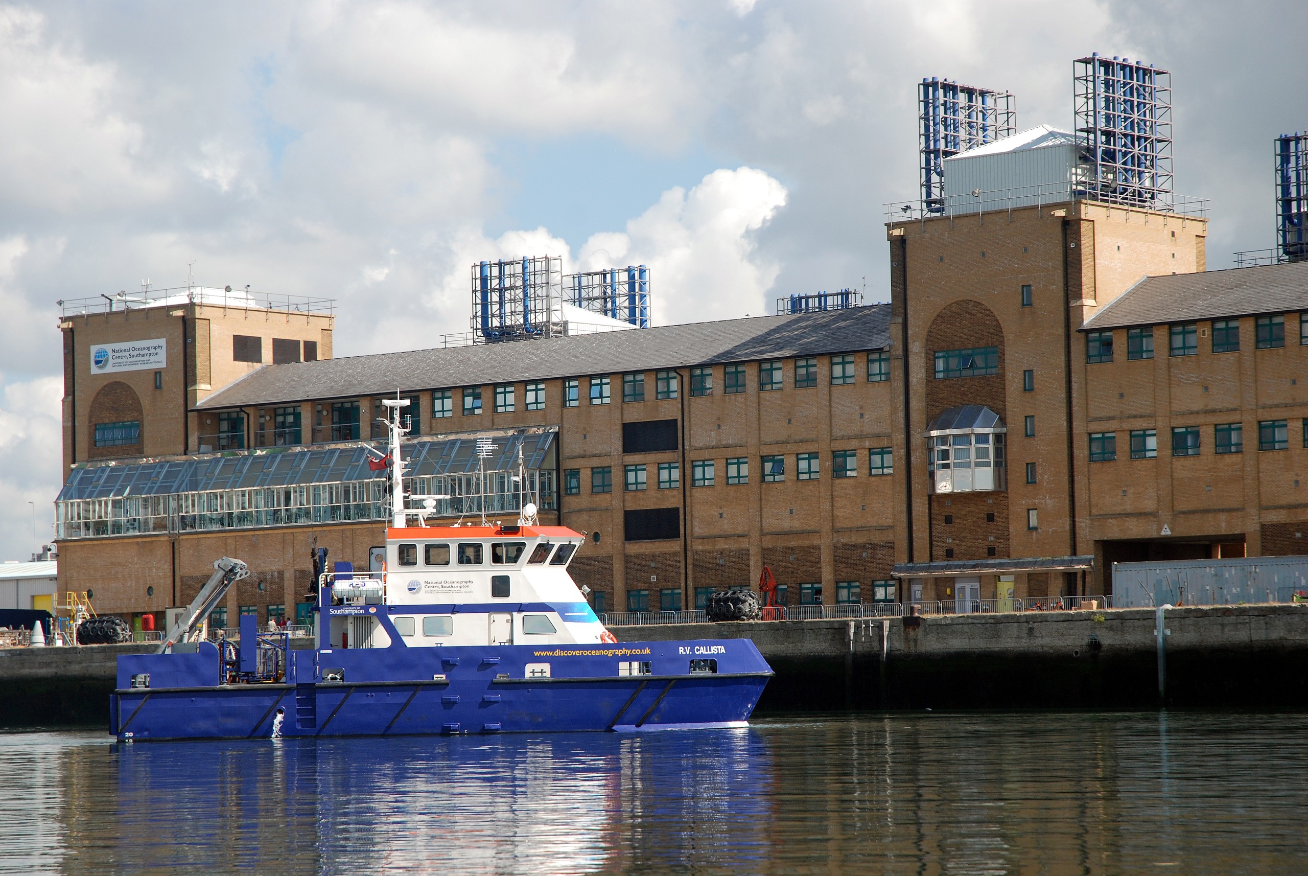 A picture of the University's Waterfront Campus building taken from the river with a blue and white boat RV Callista in the foreground.